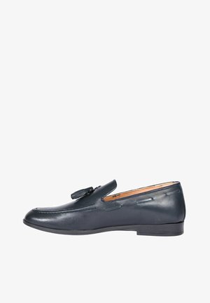 Mocassino in pelle nera con dettaglio a nappina, tacco basso e cuciture decorative lungo la parte superiore, vista laterale su sfondo bianco.