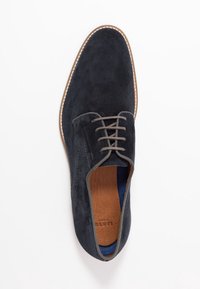 Chaussure en daim bleu foncé avec une texture lisse, bout rond et lacets gris. Présente une semelle marron avec des coutures contrastées le long du bord.