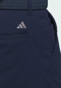 Marineblauwe sportshorts met een gestructureerde geweven riem, voorzien van een zilveren logo-detail en een zijzak. Het materiaal lijkt glad en duurzaam.