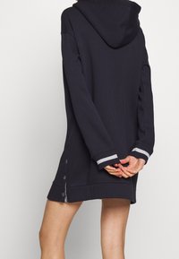 Mörkblå huvtröja i klänningsmodell med ribbade ärmslut, sidoknappar och en avslappnad passform. Mjukt material för komfort.