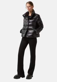 Černá prošívaná péřová bunda s lesklým povrchem, vysokým límcem a horizontálním prošíváním. Má kapsy na zip a zapínání na knoflíky.