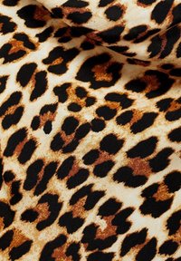 Tissu à imprimé léopard avec un fond beige ponctué de taches marron foncé et noires. Texture lisse avec des formes et des tailles de taches variées.