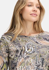Long-sleeve top featuring a colorful paisley pattern in green, black, and beige, with metallic lettering and a round neckline.
