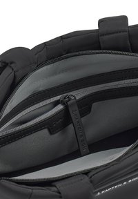 Interior de una mochila de tela negra con forro gris, que presenta compartimentos con cierre y una etiqueta etiquetada "Kapten & Son". Bordes suaves y acolchados.