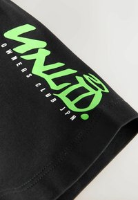 Čierne bavlnené tričko s výrazným zeleným textom a dizajnom loga. Obsahuje nápis "OWNERS CLUB JPN" v bielej farbe. Hladká textura s prešitými okrajmi.