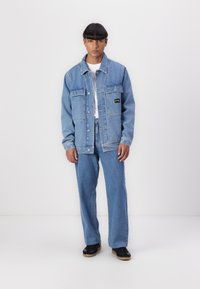 Denim jacket and jeans set in light blue. Jacket features two front pockets, button closure, and a small black label. Casual fit and texture.