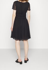 Černé šaty s krátkým rukávem, s nařaseným pasem a skládací sukní. Průsvitná vrstva, délka do poloviny lýtek, v kombinaci s černými sandály na blokovém podpatku.