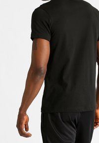 Camiseta negra de manga corta hecha de una tela suave, ajustada al cuerpo en la parte de atrás, con cuello redondo y detalles de costura sutiles.
