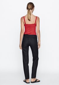 Rode geribbelde tanktop met dunne bandjes, gecombineerd met donkergrijze op maat gemaakte broek. Zichtbare zij- en achterzakken, gedragen met zwarte flip-flops.