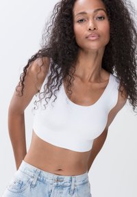 Hvid crop top lavet af strækbart materiale, med en bred udskæring og tykke stropper, parret med lyseblå high-waisted jeans.