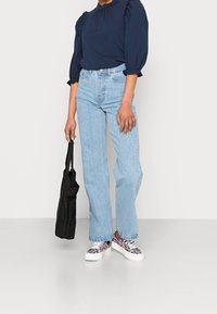 Blusa navy con maniche a sbuffo, jeans dritti blu chiaro e sneakers a fantasia. Include anche una borsa a spalla nera.