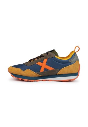 Zapatilla multicolor con parte superior de textil azul marino, acentos de ante color marrón claro, logotipo naranja brillante, talón verde y suela de goma duradera.