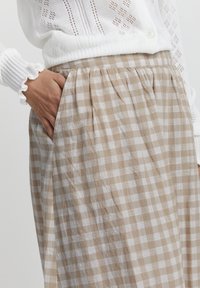 Harmaa ja valkoinen ruutuhame, joka on valmistettu kevyestä kankaasta. Hameessa on laskoksia ja sivutasku. Yläosa on valkoinen teksturoitu neule.