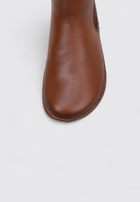 Brown leather ankle boot with a smooth texture and rounded toe. Features subtle stitching and a low-profile sole.