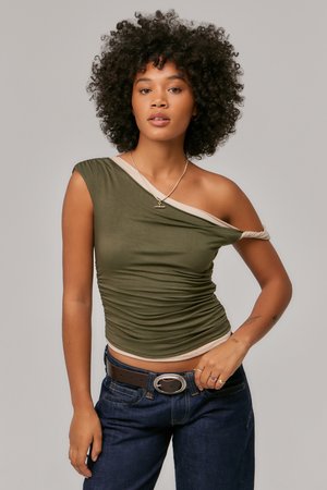 Olivengrønn, en skulder topp med asymmetrisk beige kant og samlet tekstur. Kombinert med mørk denim jeans og et brunt belte.