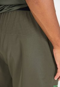Olivgröna idrottsshorts med en strukturerad, ventilerande övre del, som har små perforeringar för ventilation och ett slätt undre tyg.