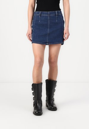 Denimrok in donkerblauw, rechte snit met een zoomlijn boven de knie. Gecombineerd met zwarte leren laarzen tot de knie met gespaccenten.