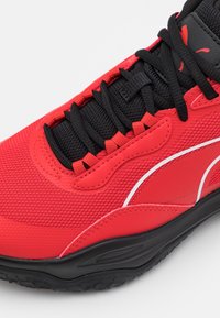 Gros plan sur une sneaker rouge et noire avec un tissu en maille, des lacets noirs et une semelle noire avec une bande d'accent blanche.