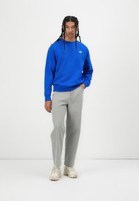 Blauwe crewneck sweatshirt met geribde manchetten, gecombineerd met lichtgrijze recht gesneden broek en beigerkleurige sneakers. Eenvoudig, casual outfit ontwerp.
