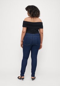 Top negro sin hombros combinado con unos vaqueros oscuros ajustados. Los vaqueros cuentan con bolsillos traseros y una textura suave.