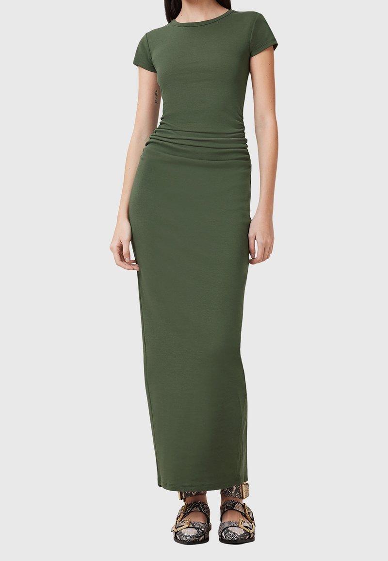 Robe maxi verte olive, ajustée, en matériau doux, avec des manches courtes et des détails froncés à la taille. Accentuée par des chaussures à motifs.