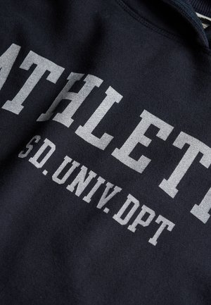 Tissu noir avec un texte imprimé blanc indiquant "ATHLETIC SD. UNIV. DPT" sur un sweatshirt plié.