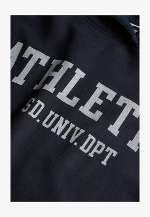 Czarna dzianina z białym nadrukiem tekstu "ATHLETIC SD. UNIV. DPT" na złożonym sweatshirtie.