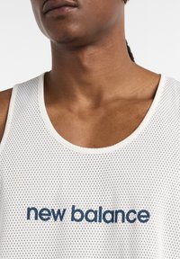White mesh tank top with a round neckline and dark blue "new balance" logo prominently displayed on the front.