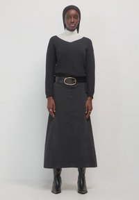 Pullover nero lavorato a maglia con un dolcevita bianco sottostante, abbinato a una gonna maxi in denim nera, cintura nera con una grande fibbia ovale e stivali al ginocchio.
