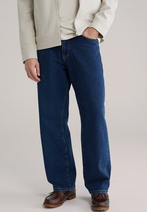 Donkerblauwe spijkerbroek met een ontspannen pasvorm, voorzien van een rechte pijpvorm en standaard vijfzakkenontwerp, gedragen met bruine schoenen.