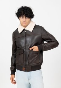 Bruine leren bomberjack met een beige schapenvachtkraag, ritssluiting aan de voorkant, twee grote zakken, geribde manchetten en een label aan de zoom.