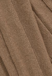 Brun stickad tyg med en texturerad, ribbad mönstring och ojämna stygn, som visar olika nyanser av brunt. Mjukt och tjockt material.