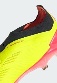 Crampon de football jaune avec tige noire, design texturé et accents roses sur la semelle. Comprend un détail de marque "HYBRIDTOUCH 2.0".