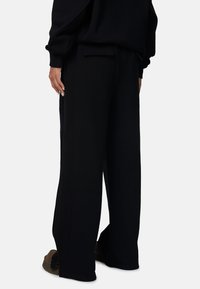 Zwarte wijde broek van zacht stof, met zijzakken en een relaxte pasvorm. Eenvoudig ontwerp zonder zichtbare patronen of hardware details.