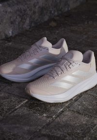 Baskets de sport rose clair avec une tige texturée, des accents blancs et une semelle épaisse. Présente trois rayures blanches de chaque côté.