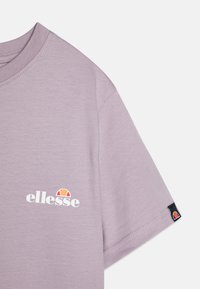 T-shirt viola chiaro realizzato in morbido cotone, con un logo grafico bianco e un piccolo logo a contrasto sulla manica. Vestibilità casual con maniche corte.