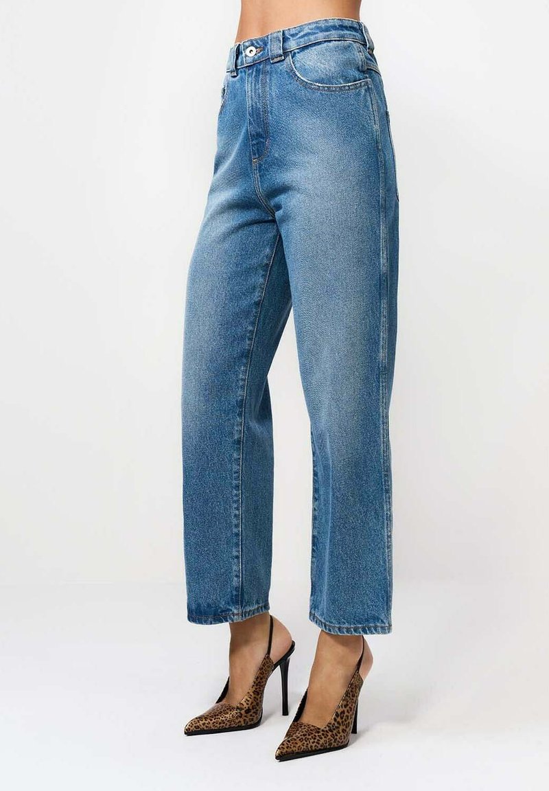 Keskmise tõusuga sirged sinised teksad, millele on sobitatud teravatele varvastele leopardimustrilised kõrged kontsad, millel on tagant kinnituvad rihmad.