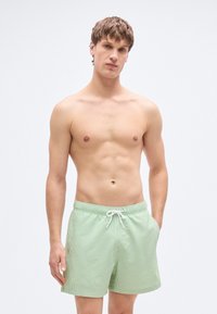 Πράσινα και λευκά ριγέ μαγιό σορτς με ελαστική μέση και κορδόνι. Ελαφρύ ύφασμα, μήκος μέχρι το μέσο του μηρού, πλαϊνές τσέπες.