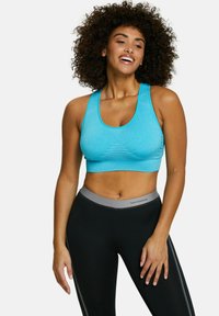 Sujetador deportivo azul claro con escote redondo y paneles texturizados, combinado con leggings negros que tienen una cintura gris y franjas laterales.