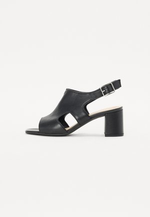 Sandales à talons en cuir noir avec bout ouvert, découpes sur les côtés et bride réglable à la cheville. Le talon bloc offre un soutien stable.