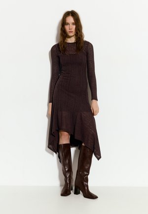 Braunes, langärmliges Strickkleid mit schwingendem Saum, strukturiertem Material und geschichteter Gestaltung. Kombiniert mit braunen, kniehohen, gestuften Stiefeln.