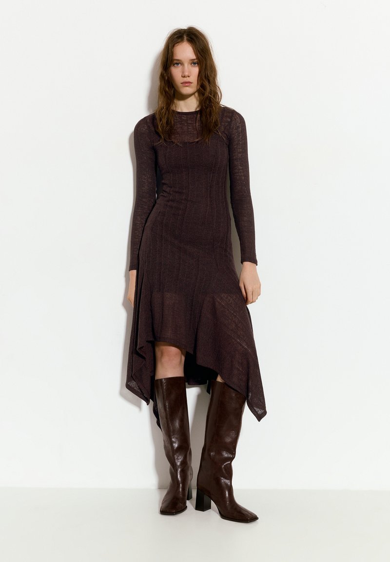 Brun, langærmet strikkjole med flared kant, tekstureret materiale og lagdelt design. Parret med brune støvler med hæl, der går op til knæet.