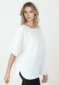 Witte, losse blouse met pofmouwen en een gebogen zoom. Zachte textuur en gladde stof. Gecombineerd met zwarte legging.