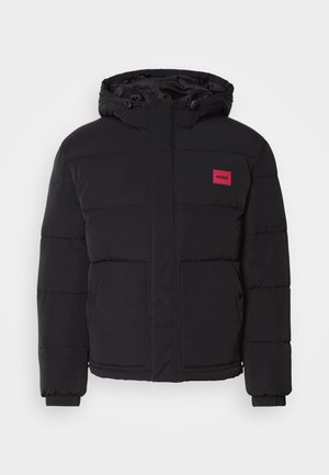 Black puffer jacket with a hood, featuring a red logo patch, quilted pattern, front pockets, and elastic cuffs for warmth and comfort.