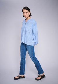 Camisa de rayas azul claro con un corte relajado, combinada con jeans azul oscuro y chanclas negras. Diseño sencillo con un escote sin cuello.