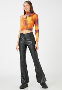 Crop-Top in Orange und lila Batik, mit hohem Kragen und Cut-Out-Detail, kombiniert mit schwarzen, kunstledernen, ausgestellten Hosen und klobigen schwarzen Stiefeln.
