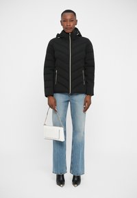 Black padded jacket with a hood, featuring a chevron design, gold zippers, paired with light blue flared jeans and a white handbag.