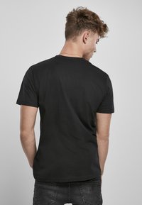Czarny bawełniany t-shirt z krótkimi rękawami, okrągłym dekoltem, gładką fakturą i luźnym krojem, widok z tyłu.