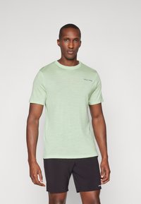 T-shirt de manga curta verde claro em tecido suave, com gola redonda e uma discreta marcação azul no peito. Combinado com calções pretos.