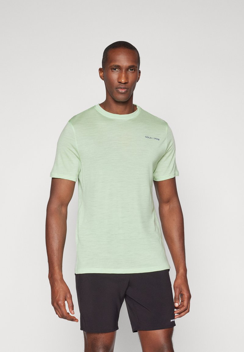 T-shirt de manga curta verde claro em tecido suave, com gola redonda e uma discreta marcação azul no peito. Combinado com calções pretos.